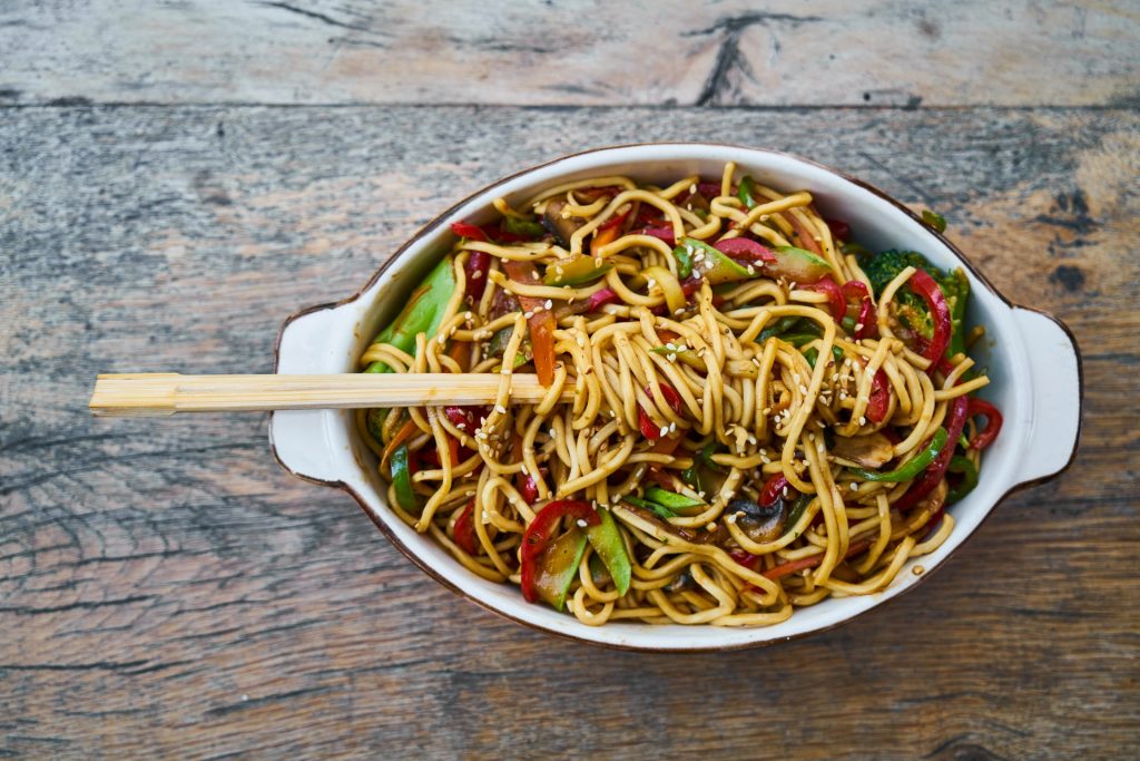 A top view of the bowl of yummy pasta made with vegetables on a wooden table top
