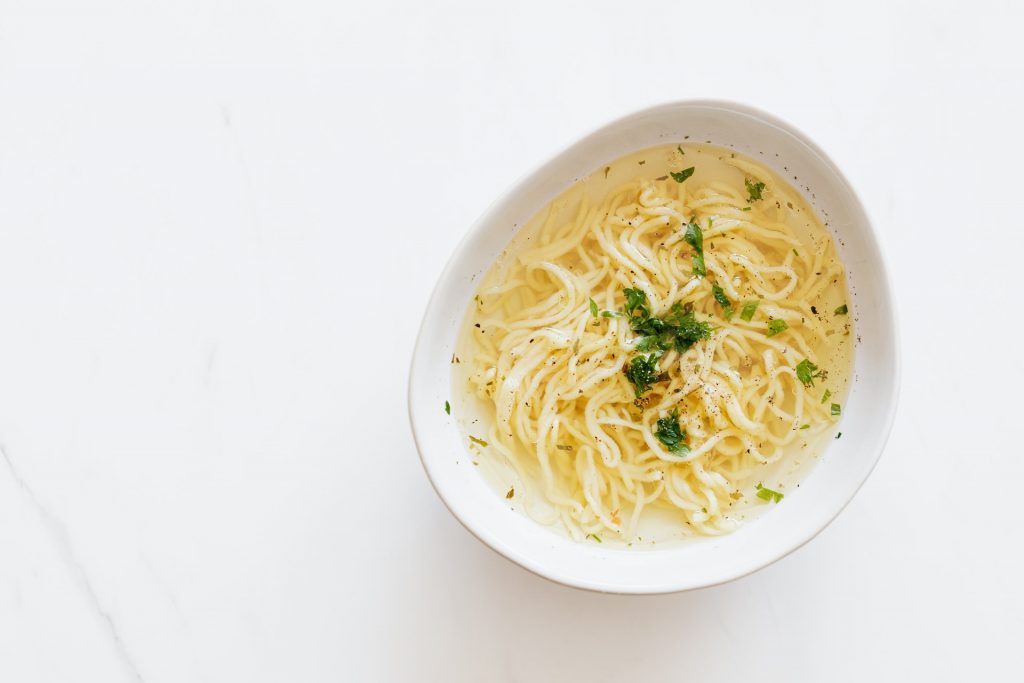A photo top view of the white bowl of chicken noddle soup on white background
