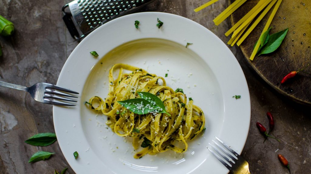 A white bowl of cooked spaghetti on the table with fork and other utensils