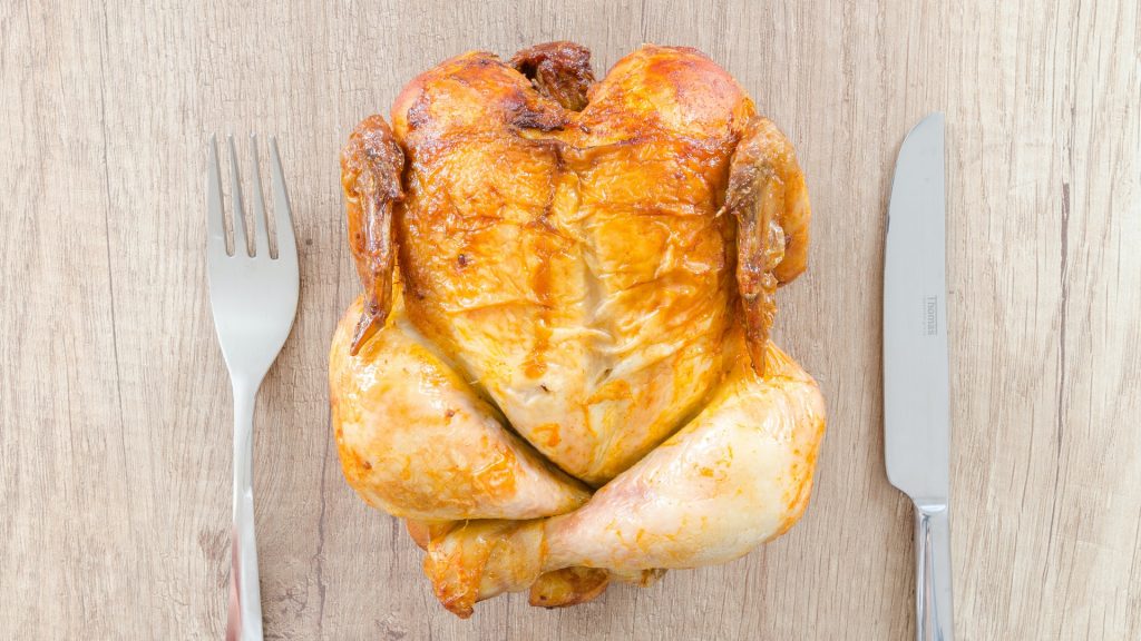 Rotisserie Chicken on the wooden table with knife and fork on both sides.