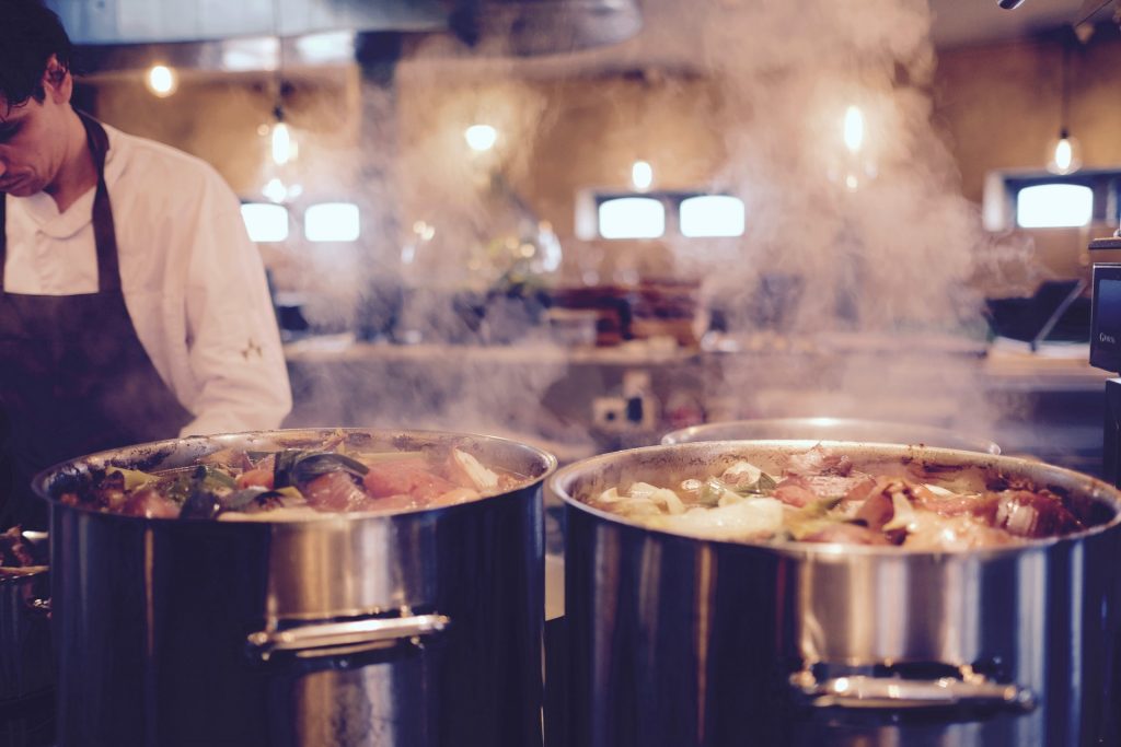 Two metallic pots with steamy boiling soup at the commercial or restaurant kitchen