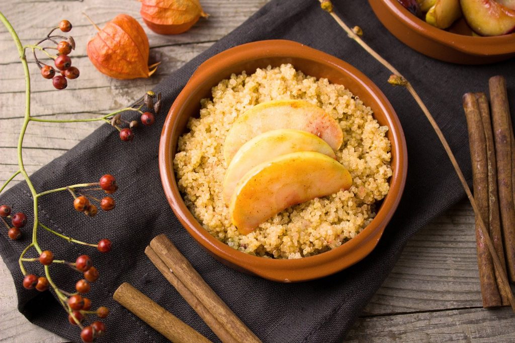 A top view of brown bowl with cooked quinoa and some tortias on top of wooden table.