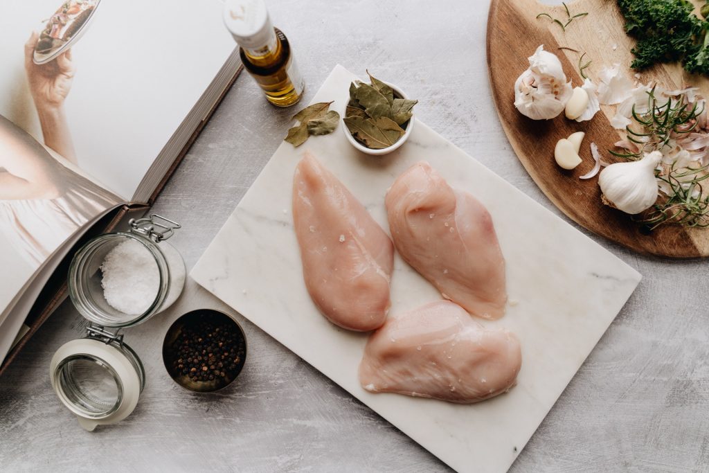 An uncooked chicken meat pieces on a wooden cutting board on the table top with few spices around