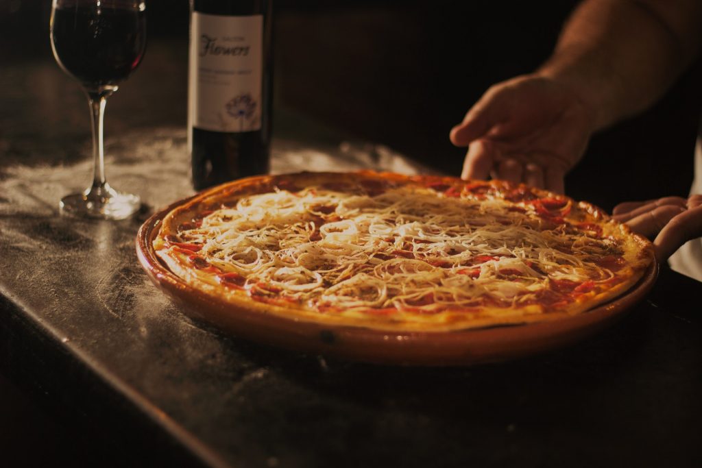 Fresh made pizza with pizza sauce and cheese on it, on the table, and a bottle of red wine.