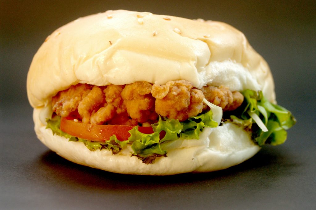 A chicken sandwich, white bread bun and crispy fried chicken with green salad leaf on dark background.