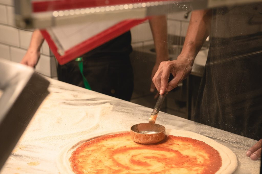 Cook putting pizza sauce on top of pizza dough before baking