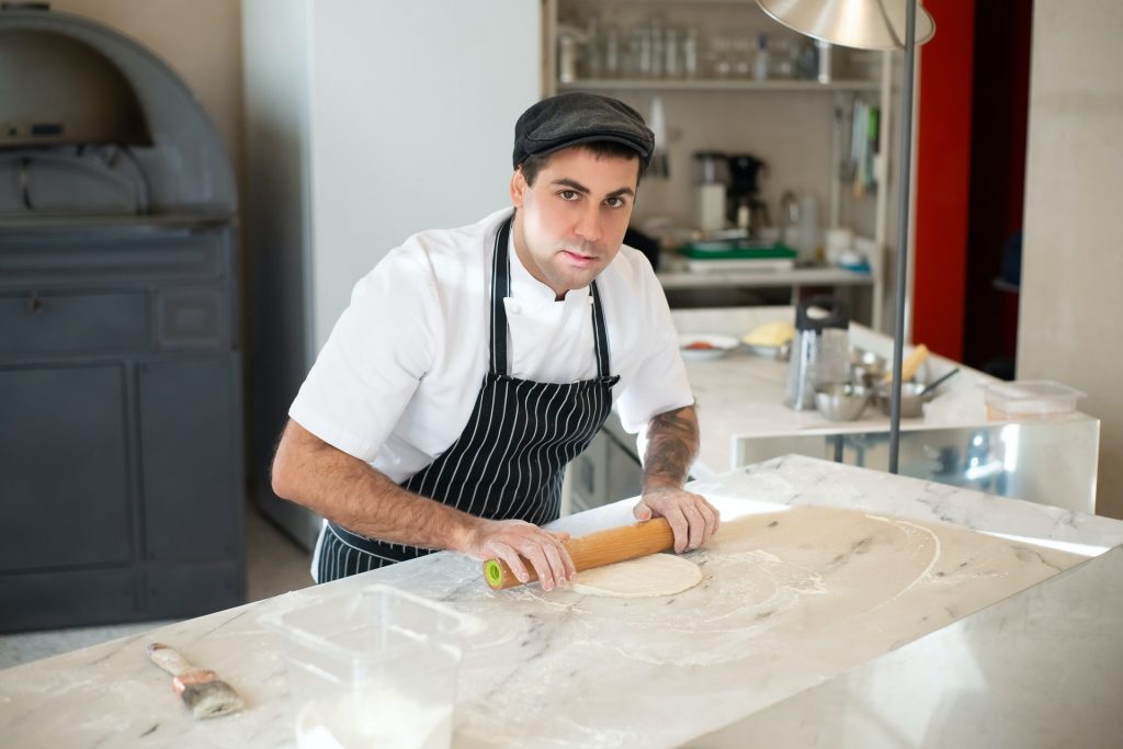 A cook is kneading pizza dough on the wooden table