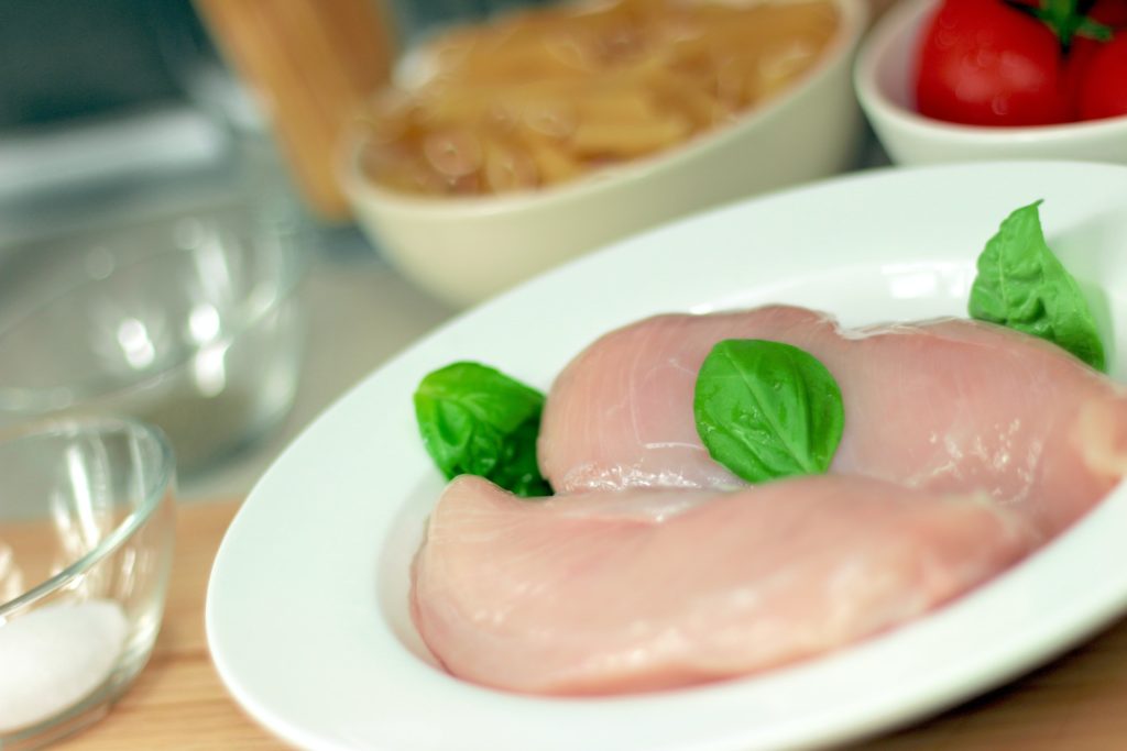 Uncooked pink chicken meat pieces on white plate on a table