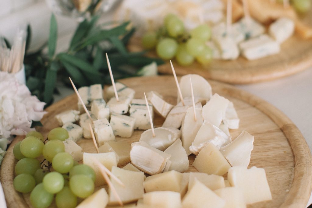 Many cut cubes of different variety of cheeses with toothpicks stuck in them and green grapes served on wooden round trays - how to serve different types of cheeses