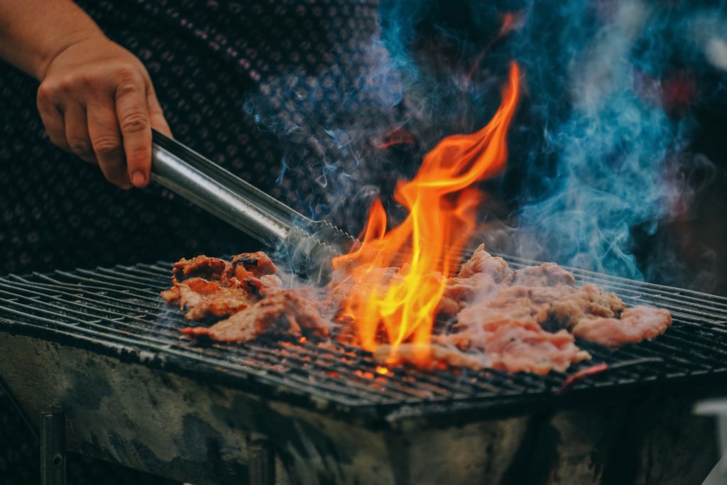 A person is grilling meat on the grill on open fire