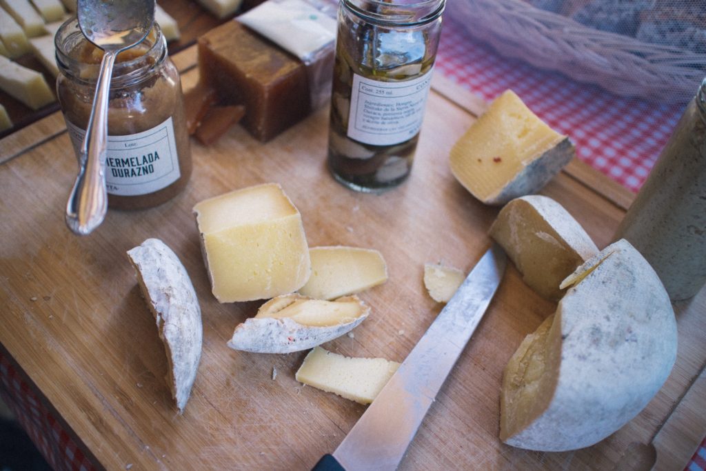 Several cut pieces of cheese lying on the wooden table right by the main cheese block along with two jars of sauce Easy Cheese Snacks to Make at Home