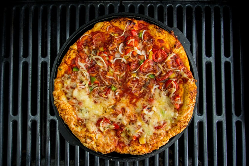 A yellow cheesy pizza with lots of tomatoes laying on top of the grill grates, pizza, grill pizza, grill, grilling