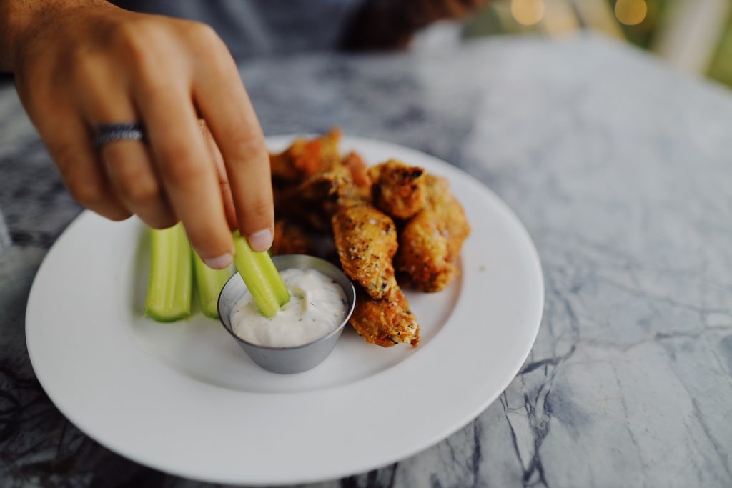 Hot chicken wings with traditional celery and blue cheese dip on the white plate, a persons hand dipping celery into the dip, food, dinner, chicken, eat, cook