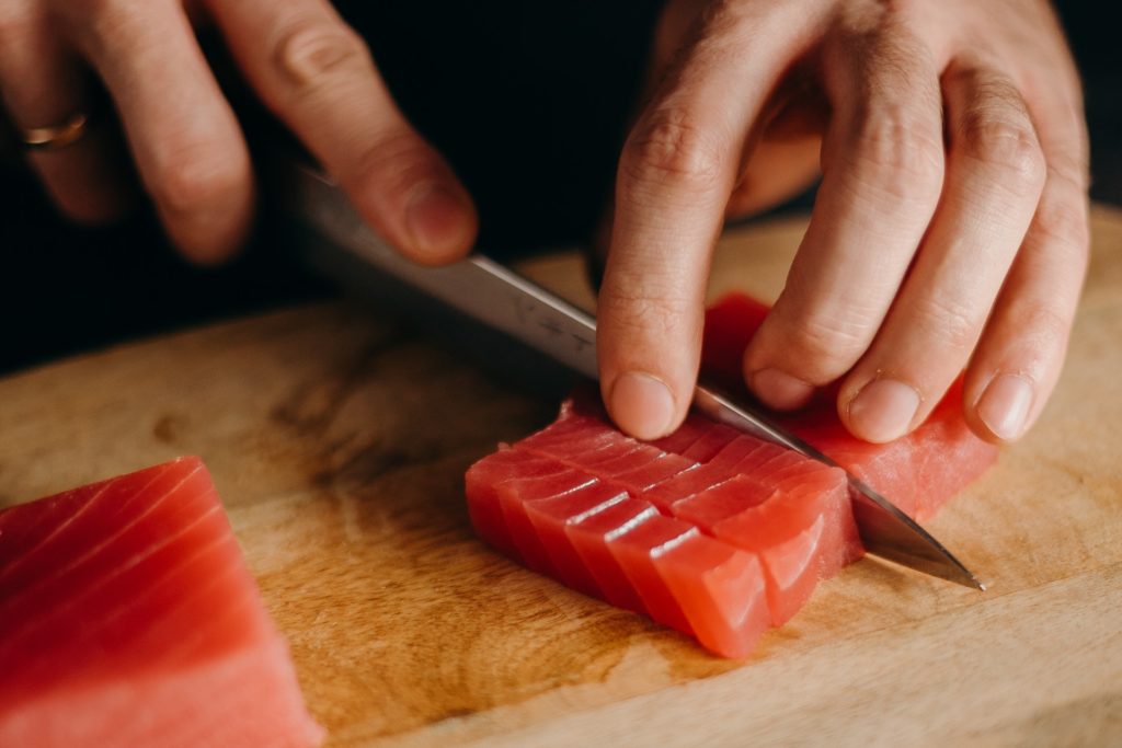 A sushi chef cutting red fish for sushi with the knife of wooden cutting board, sushi, preparing sushi, fish, preparing fish for sushi