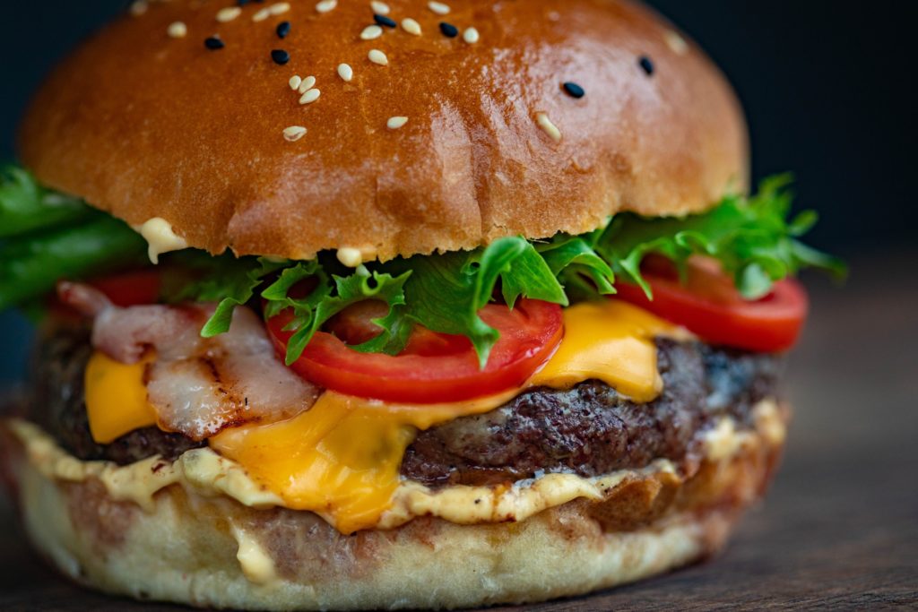 A large burger with meat patty, melted cheese, tomatoes and salad leaves, on a dark background. Burger, Hamburger, Cheeseburger, how to make a burger.